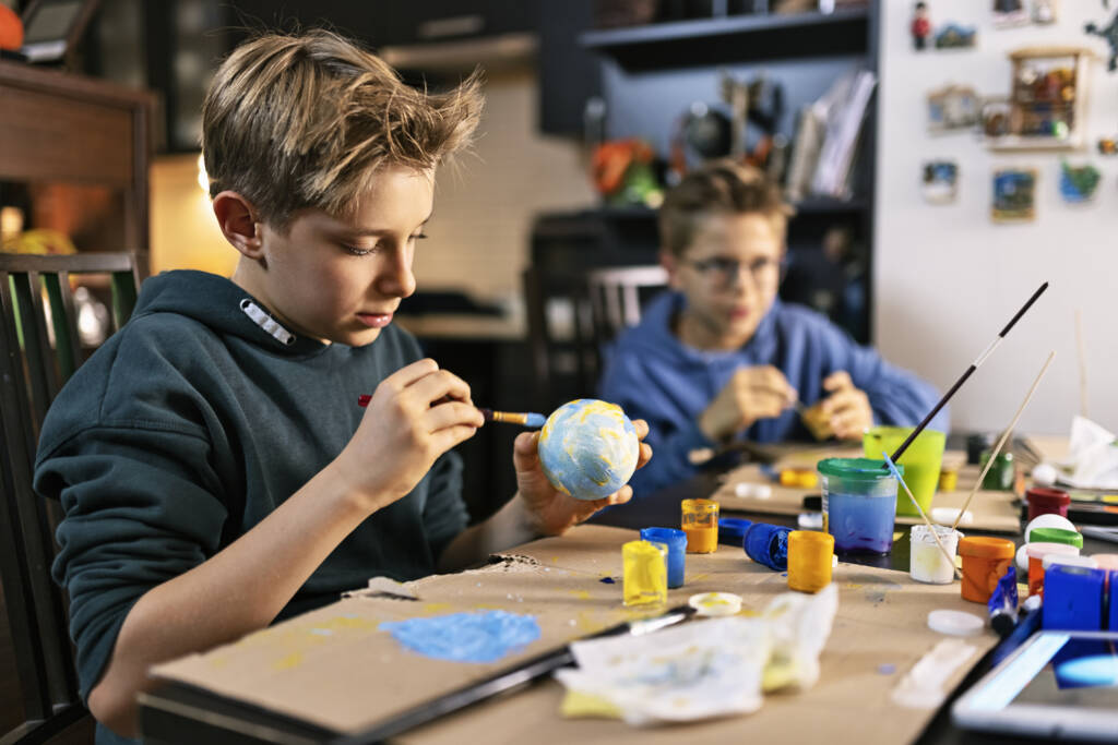 boys making solar system project at home. The boys are painting sun and planets. One of the boys is painting the planet Earth.