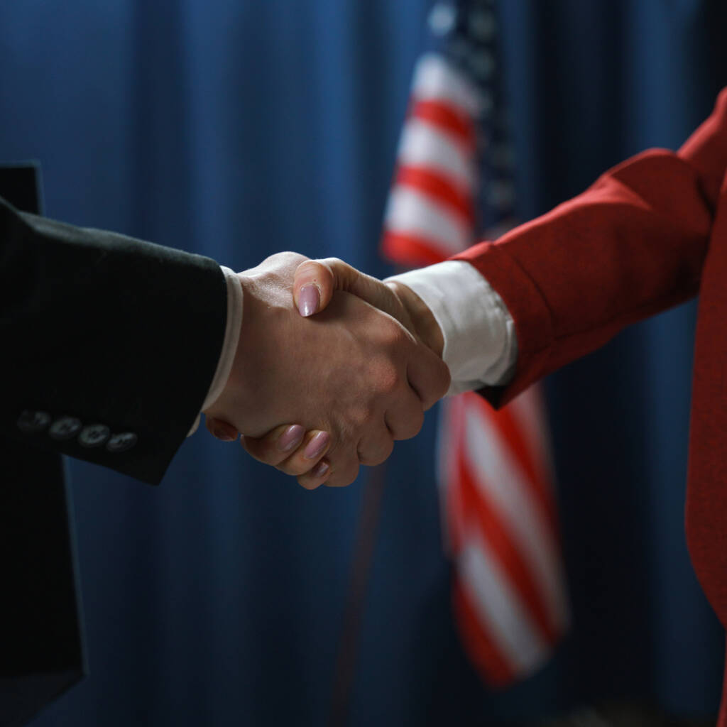 Close-up of a handshake of a man and a woman politicians on a blue background with a US flag