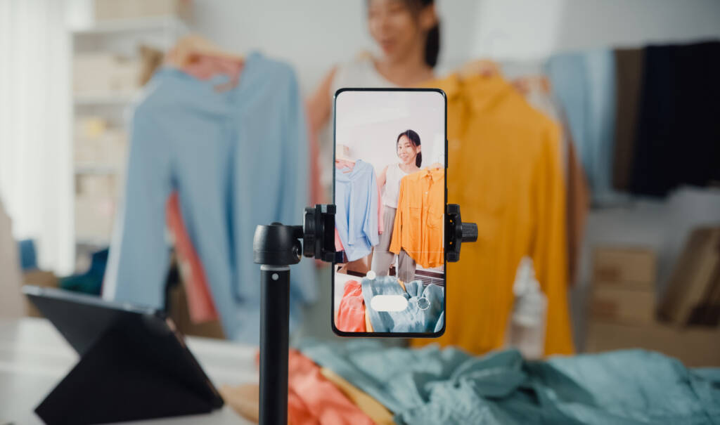 woman live-streamed ecommerce sell clothes at home, girl using the smartphone and tablet for recording video.