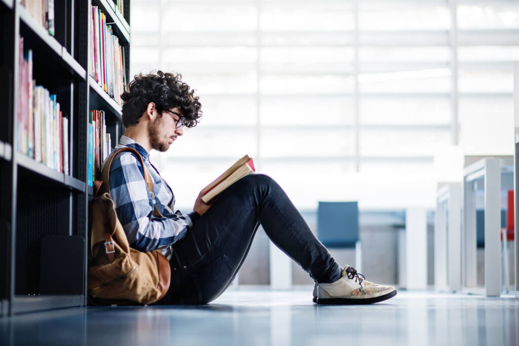 male student reading a book in a library.
