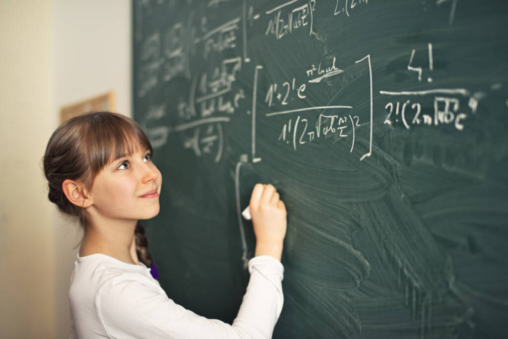 girl writing difficult mathematics equations on a green chalkboard.