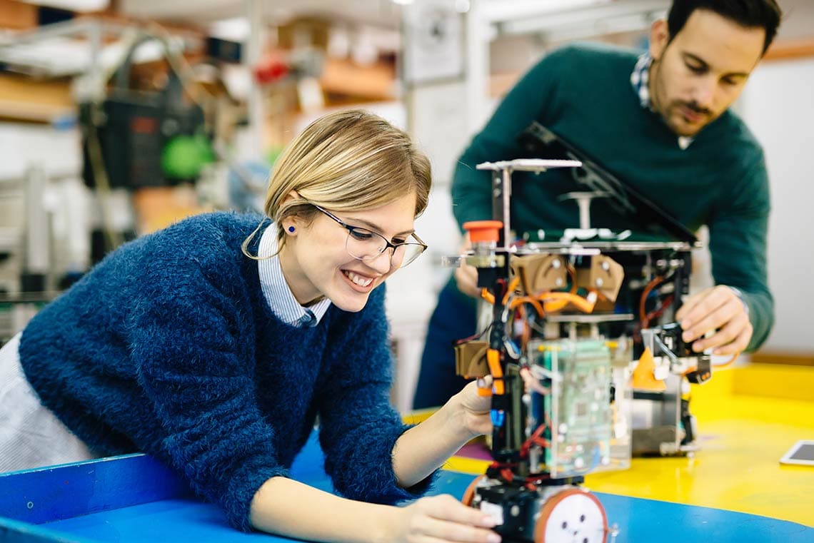 Two students work together on a robotics project in a workshop setting.
