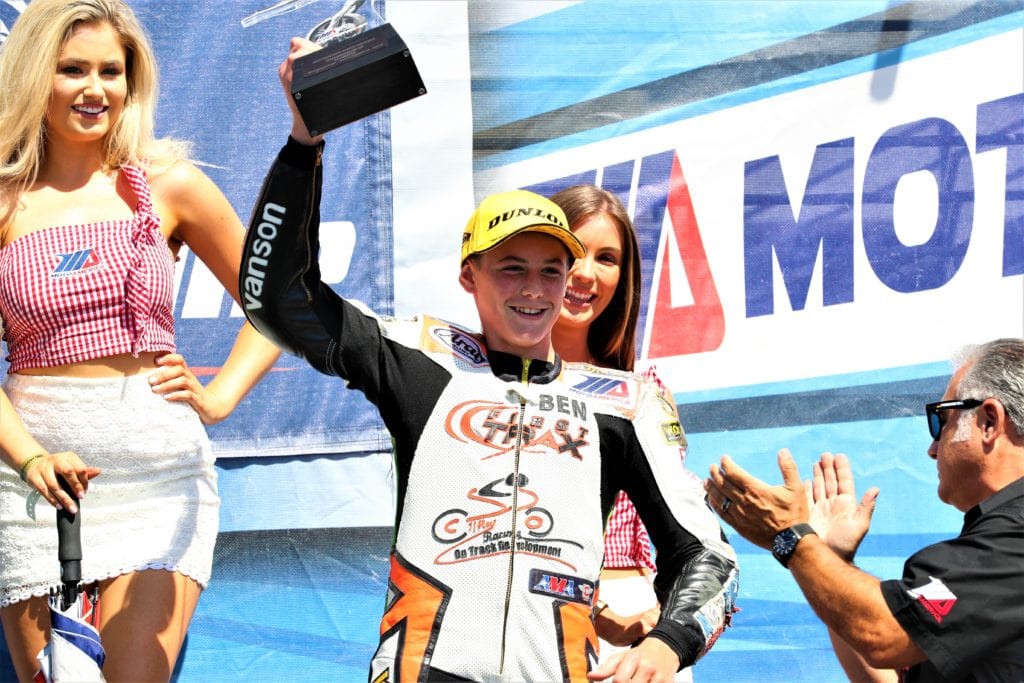male competitive motorcycle racer holding trophy on podium