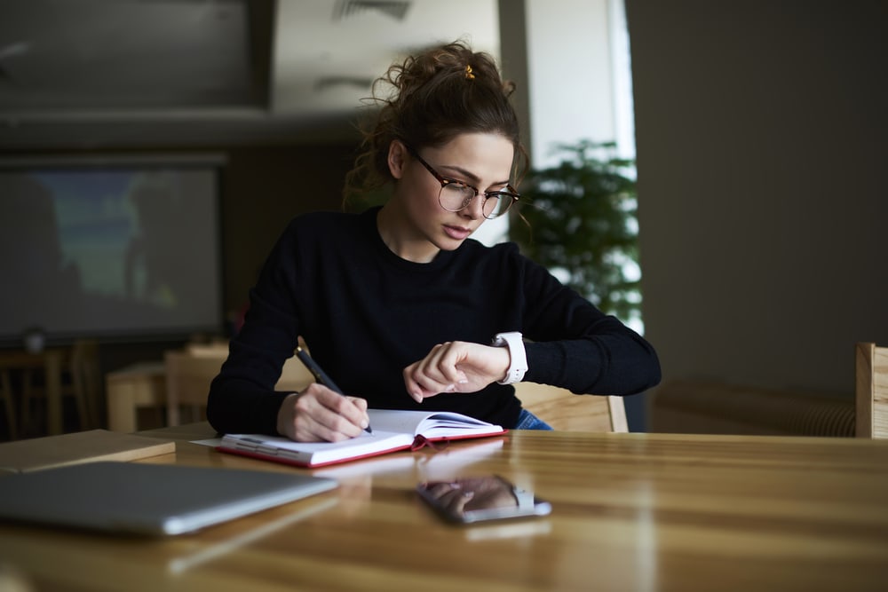 female looking at her watch while jotting down notes
