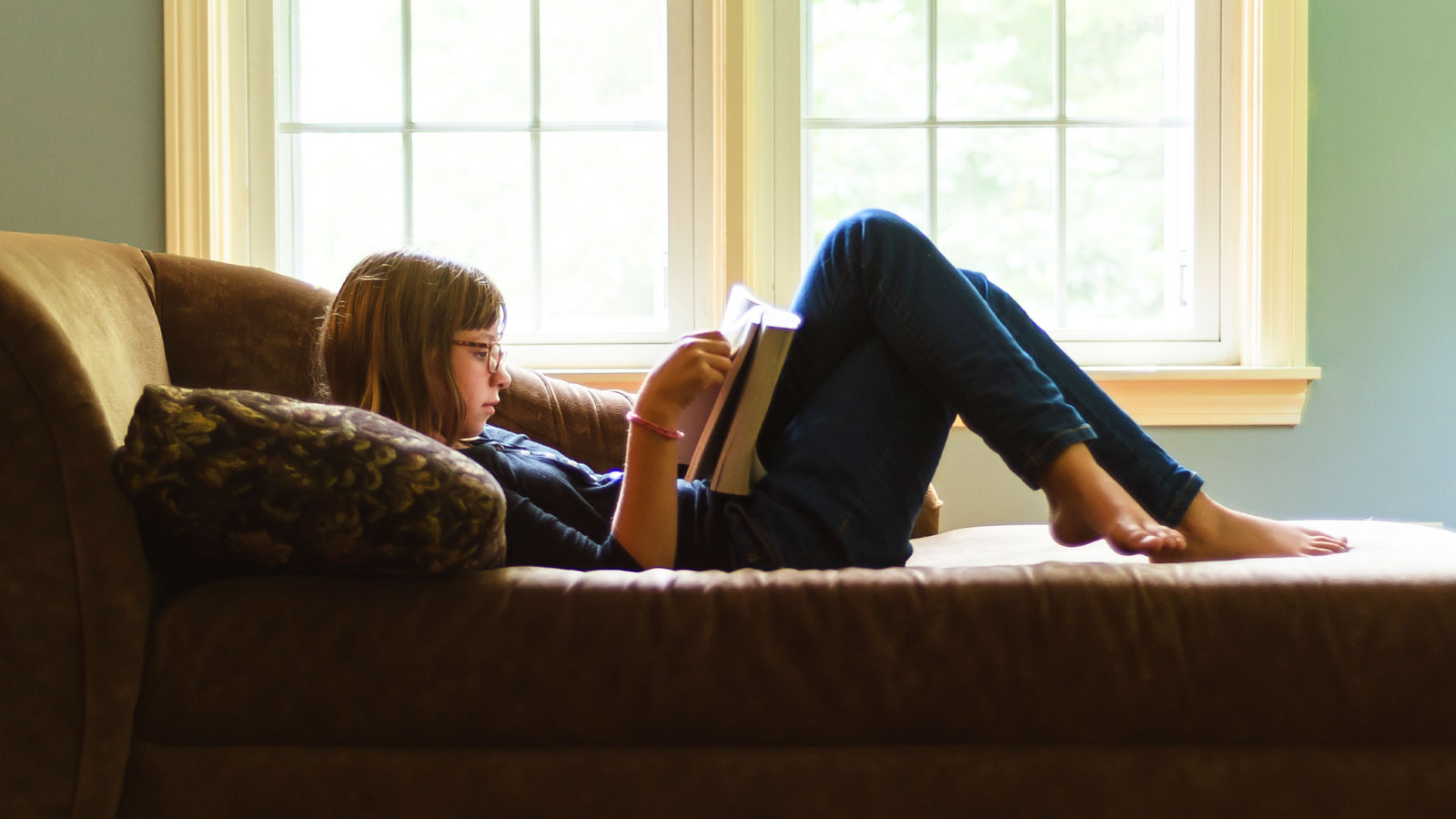 middle school girl reading at home on couch
