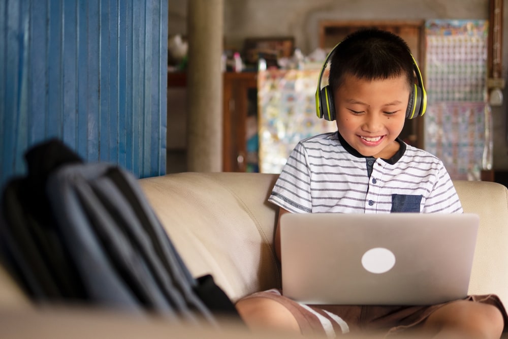 child on laptop computer with headphones smiling