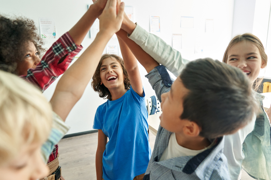 Group of children giving a high-five together in a classroom.