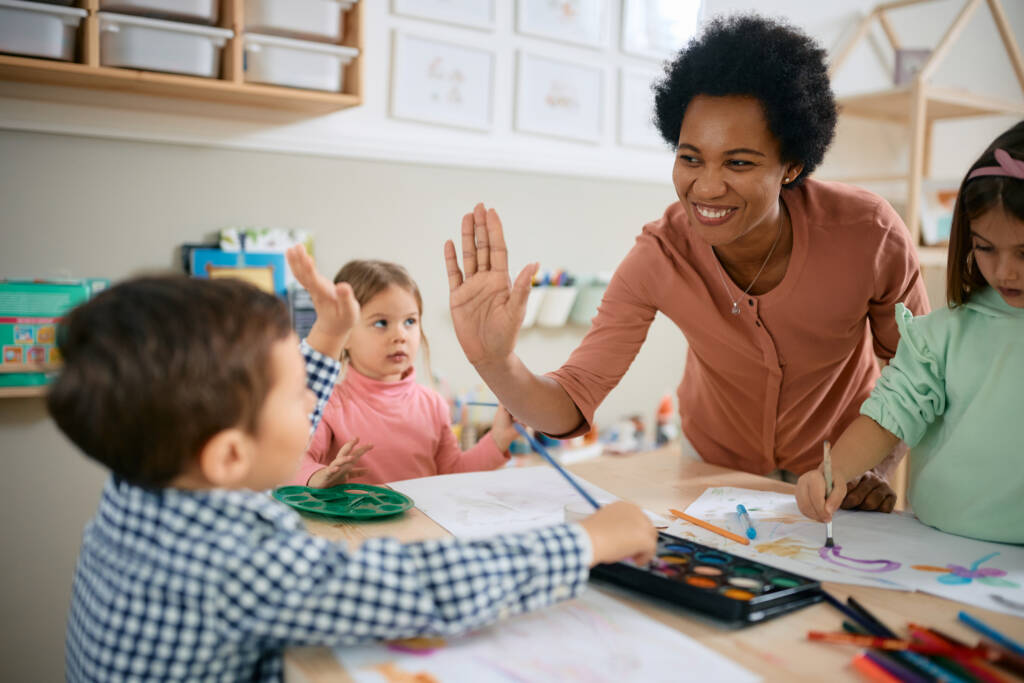 teacher and small boy giving high-five during art class at kindergarten.