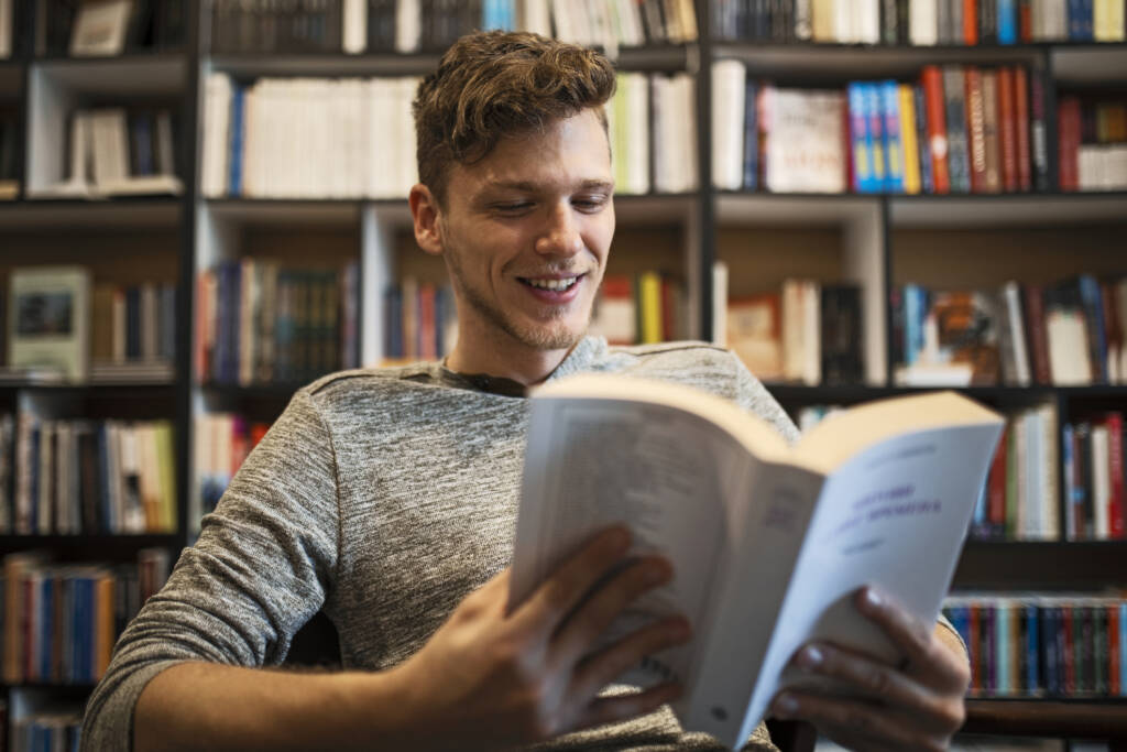 Student in library reading book from bookshelf