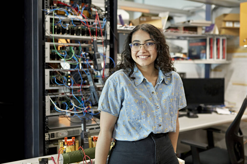 woman standing in electrical engineering lab and smiling at camera.